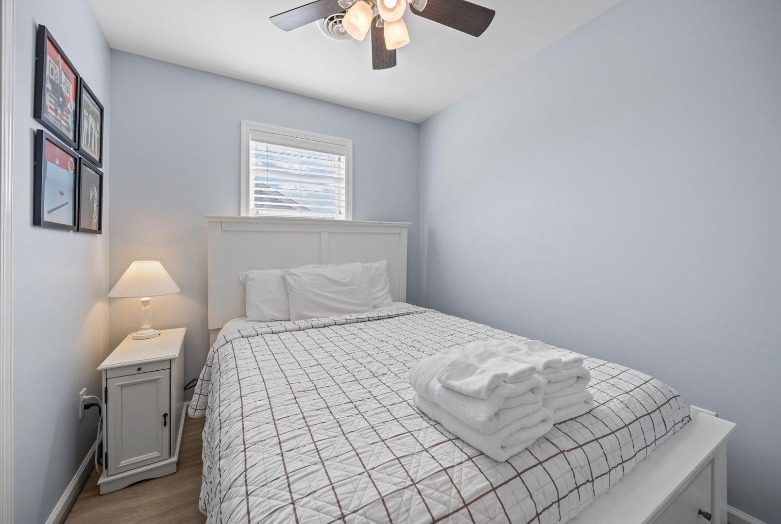 A bedroom with a bed, a nightstand, a lamp, a ceiling fan, and a window.