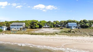 A beachside property with multiple houses, a sandy beach, and a clear sky. - Whispering Oaks 3 Bedroom Home by RedAwning (Harkers Island)