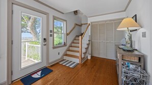 A staircase leading to a second floor, a wooden door with a view of the outdoors, and a lamp on a console table. - Whispering Oaks 3 Bedroom Home by RedAwning (Harkers Island)
