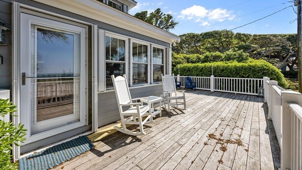 A wooden deck with white chairs and a table, a white fence, and a view of the sea. - Whispering Oaks 3 Bedroom Home by RedAwning (Harkers Island)