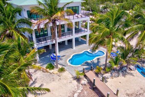 A two-story building with a pool, surrounded by palm trees and a sandy area.
