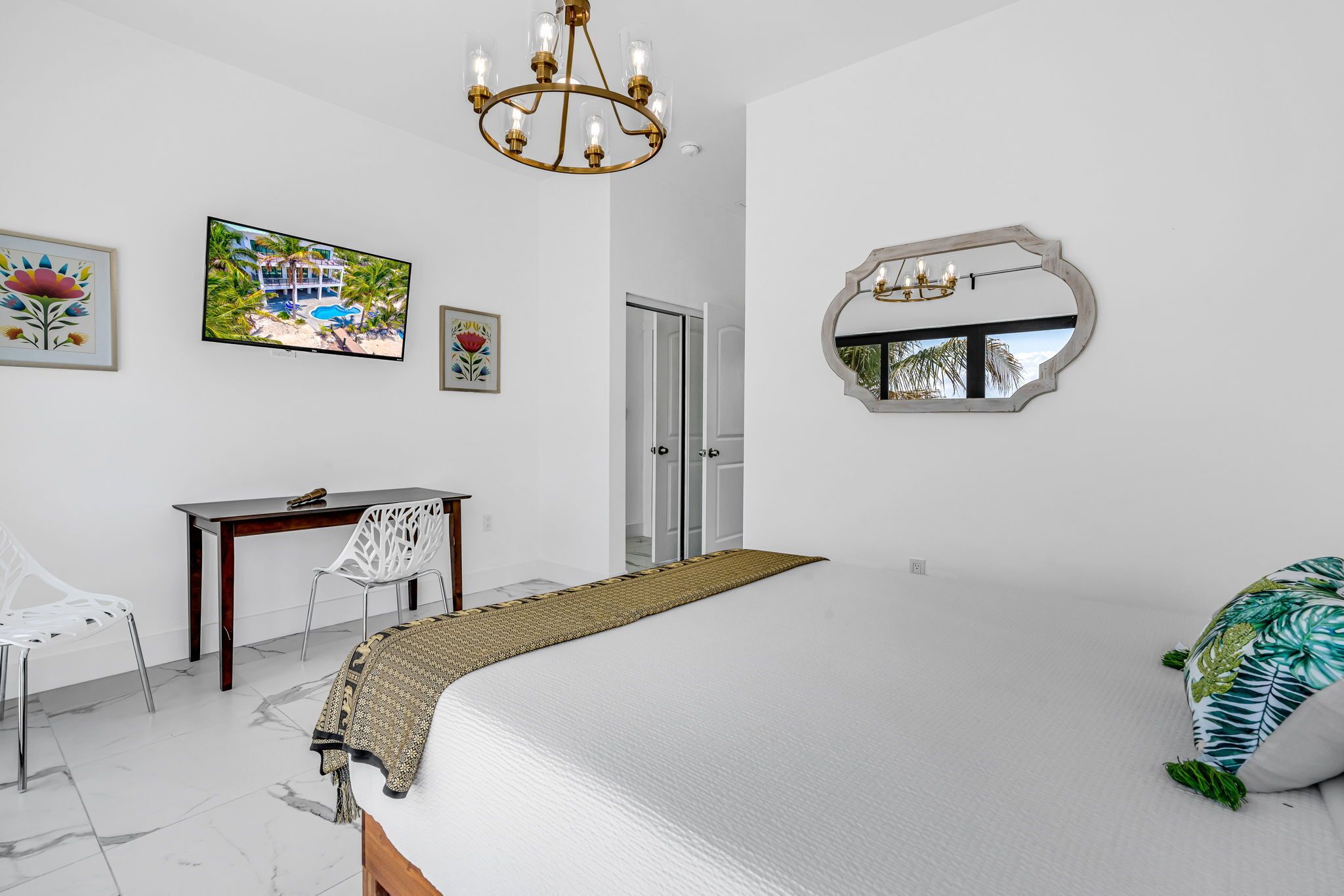 A bedroom with a large bed, a desk with a chair, a television, and a mirror on the wall.