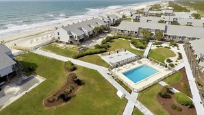 Vista aérea de un complejo turístico con piscina, acceso a la playa y varias construcciones.