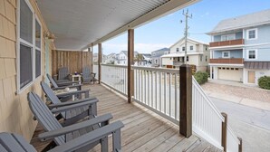 Eine überdachte Veranda mit Holzgeländern, mehreren Adirondack-Stühlen und Blick auf benachbarte Häuser.