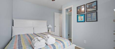 Une chambre à coucher comprenant un lit, un ventilateur de plafond, une table de chevet et une porte donnant sur une autre pièce.