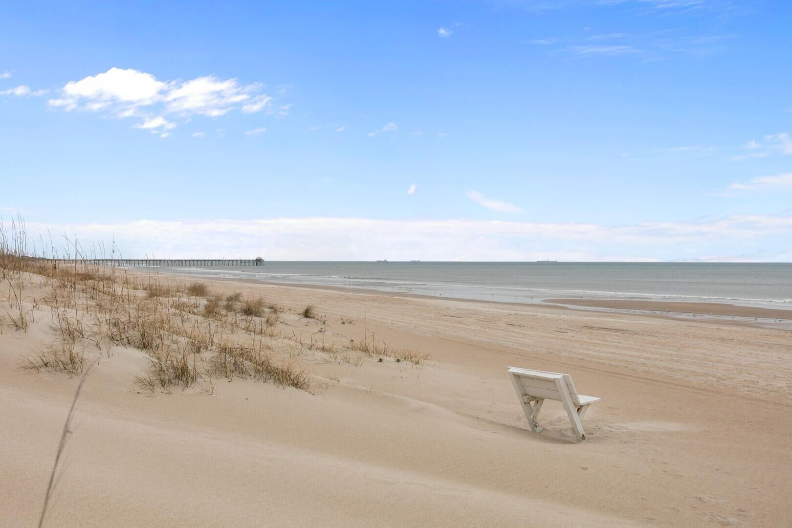 A beach with a white bench and a pier in the background.