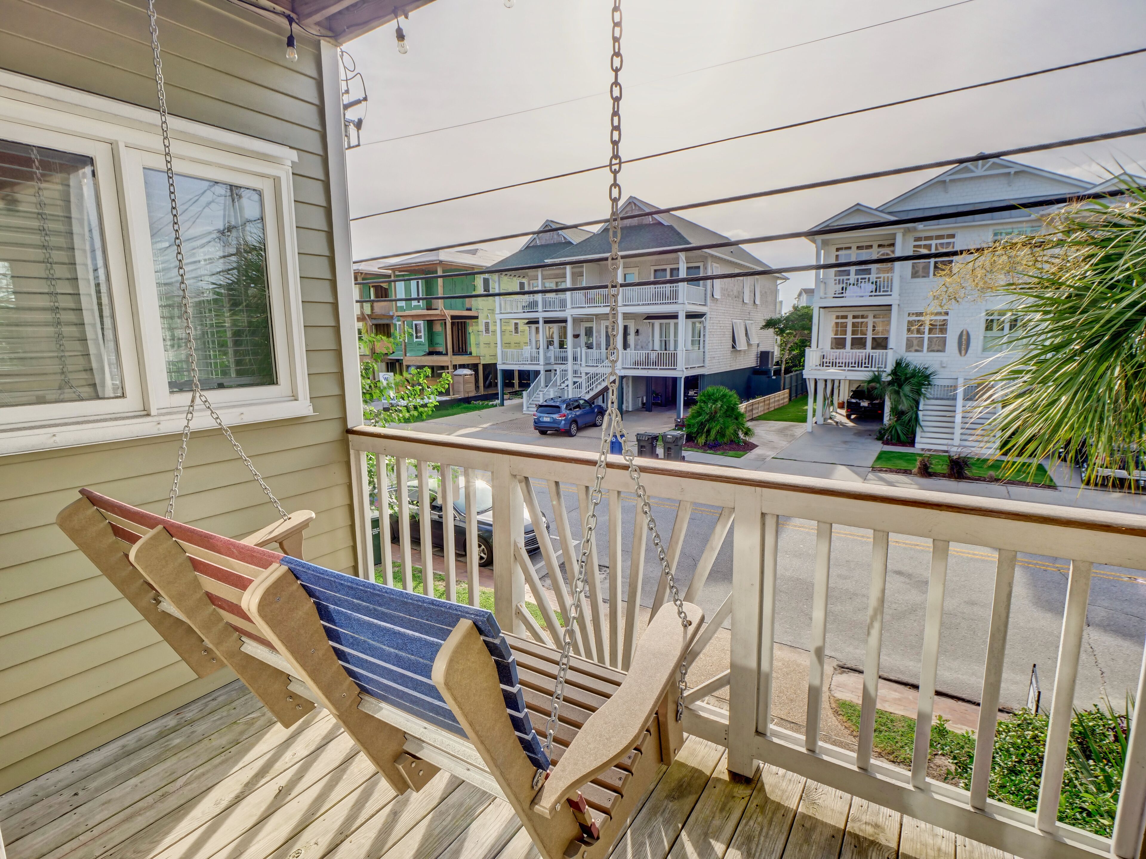 A wooden porch with a swing, overlooking a street with multi-story houses.