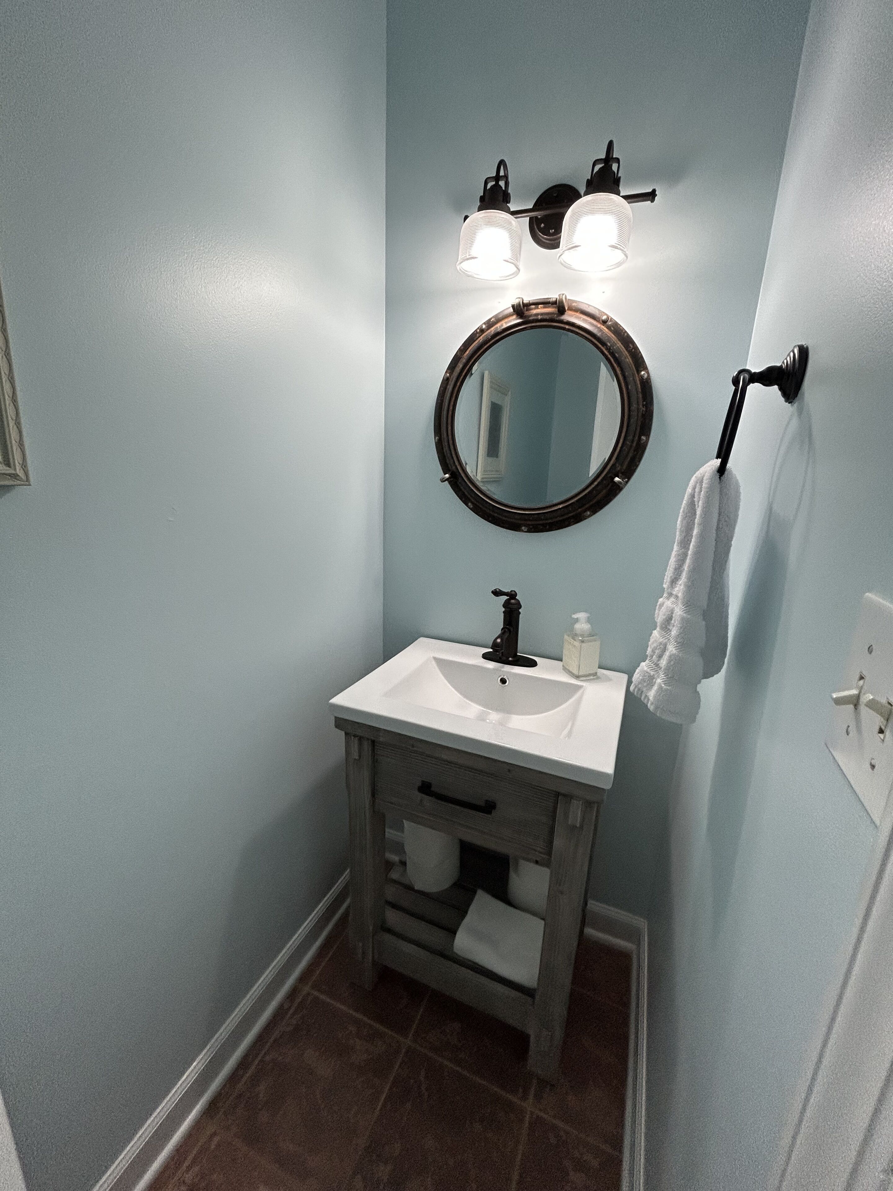 A bathroom with a white sink, a round mirror, and two wall-mounted lights.