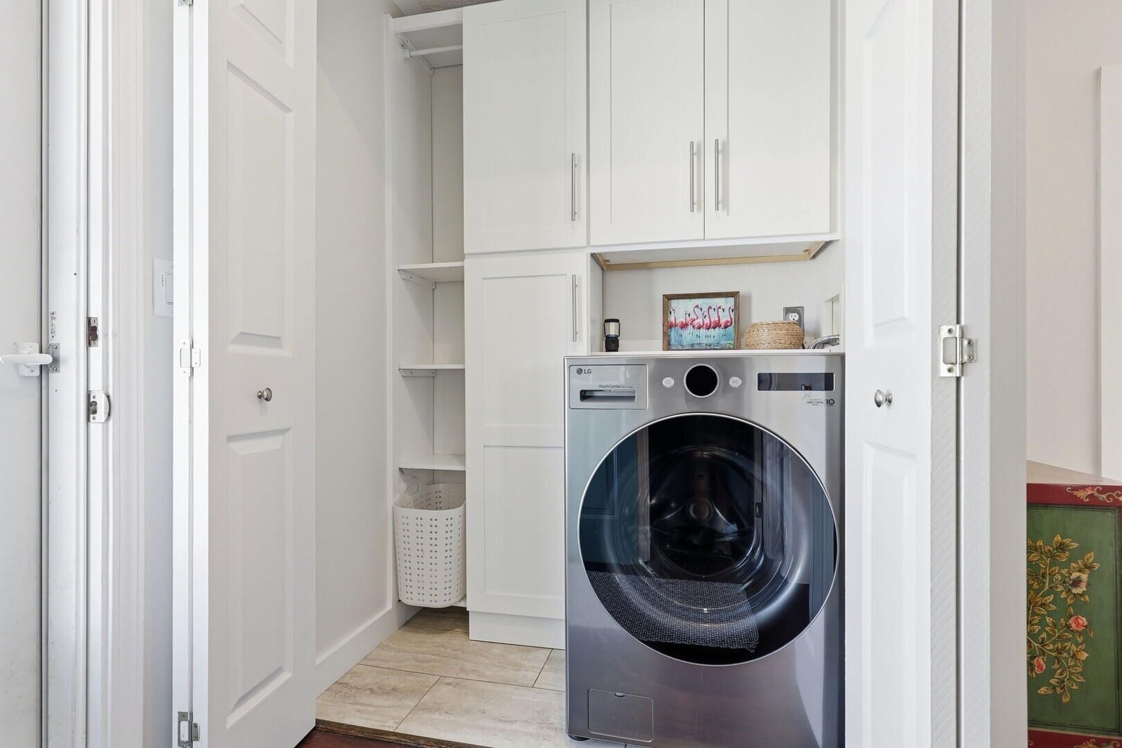 A laundry room with a front-loading washing machine, white cabinets, and a basket.