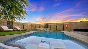 A swimming pool with lounge chairs and a table with glasses, surrounded by a brick wall and a sunset view. - Buddha Estate#4 - Great neighborhood, Sparkling pool and Hot tub, EV Charger, Games (Henderson)