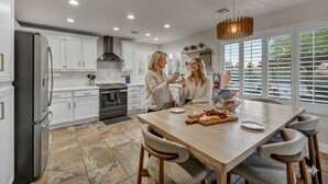 A modern kitchen with white cabinets, a stainless steel refrigerator, and a dining area with a wooden table and chairs. - Buddha Estate#4 - Great neighborhood, Sparkling pool and Hot tub, EV Charger, Games (Henderson)