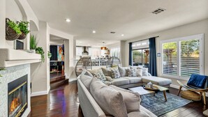 A modern living room with a sectional sofa, a fireplace, and a view of the kitchen and dining area. - Buddha Estate#4 - Great neighborhood, Sparkling pool and Hot tub, EV Charger, Games (Henderson)
