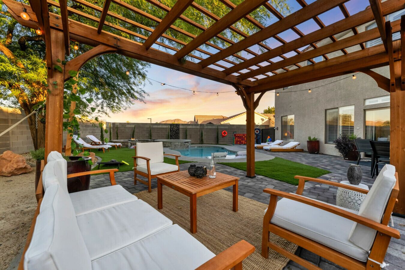 Un patio techado al aire libre con muebles de madera, piscina y vistas a una casa moderna.