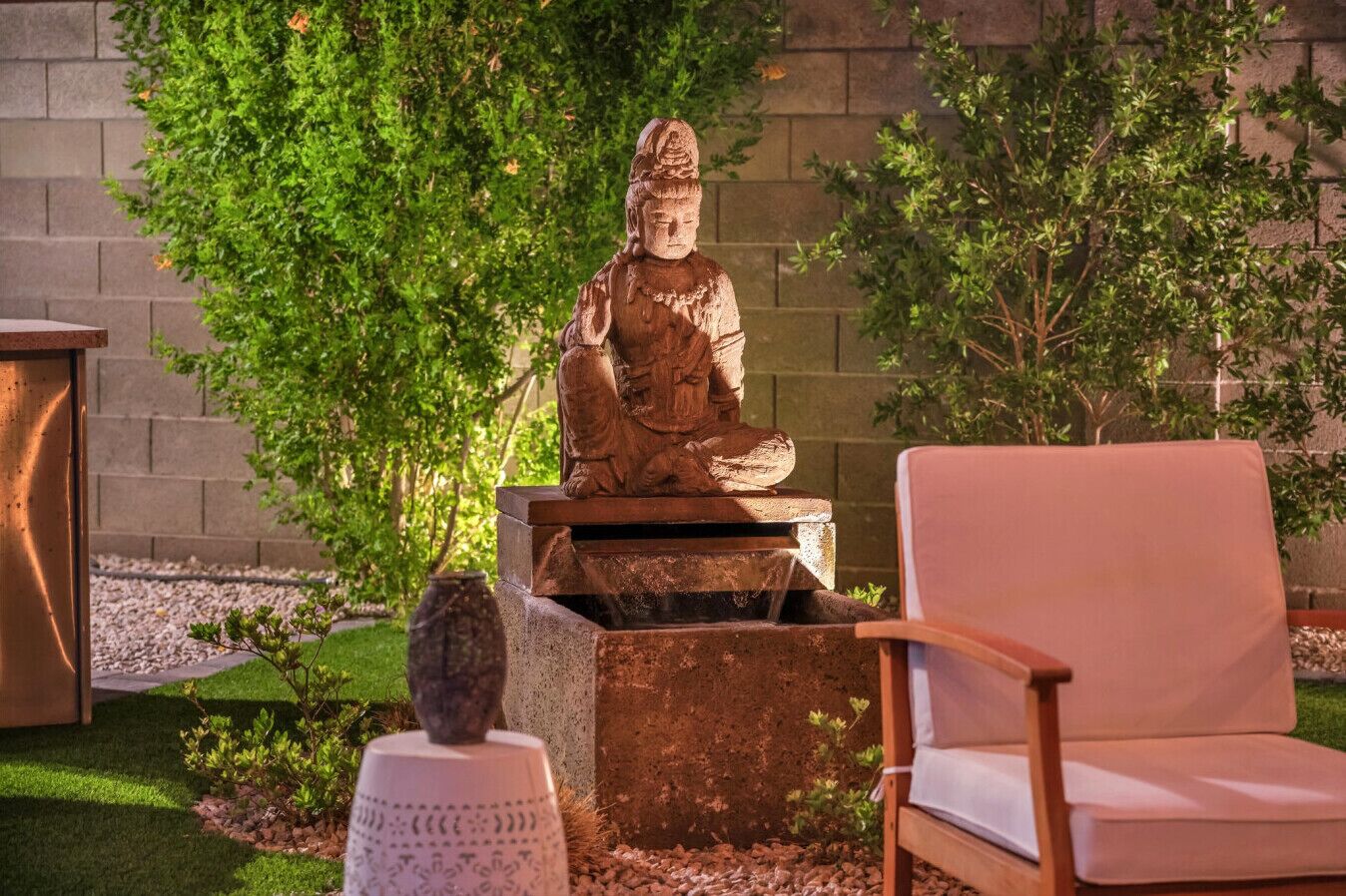 Une statue représentant une figure assise, une chaise blanche et un petit objet décoratif.