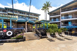 A hotel with multiple balconies, a pool area with lounge chairs, and a stone wall with a lifebuoy. - NEW, BEACHFRONT KONA REEF ALOHA CONDO WITH A/C (Kailua-Kona)