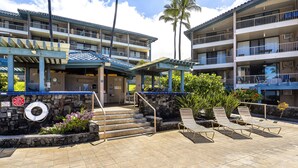 A hotel with multiple balconies, a pool area with lounge chairs, and a stone wall with a lifeguard ring.