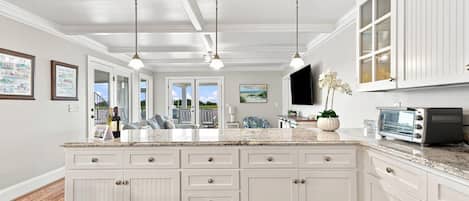 A kitchen with a large island, white cabinetry, pendant lighting, and a flat-screen TV mounted above the island.