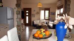 A living room with a sofa, a dining table with fruit, and a blue vase. - Anastasia s Cottage in Pelion (Zagora-Mouresi)