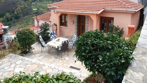 A house with a tiled roof, stone patio, and a table with chairs. - Anastasia s Cottage in Pelion (Zagora-Mouresi)