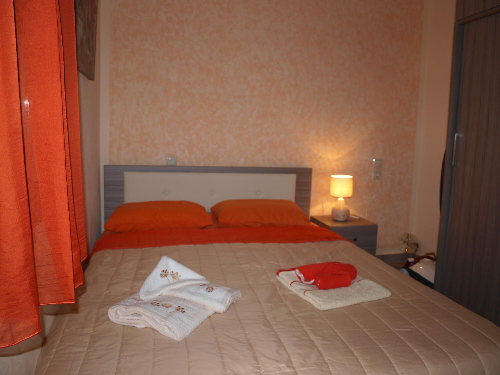 A hotel room with a bed, orange pillows, a bedside lamp, and neatly folded towels on the bed.