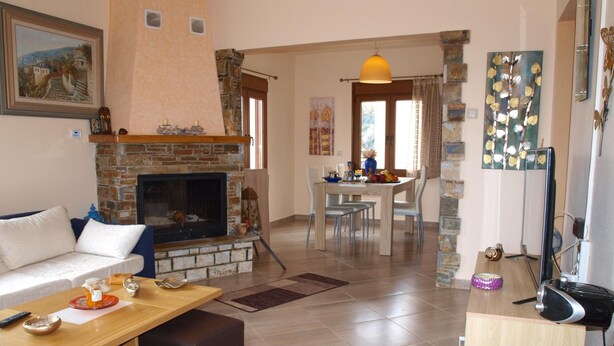 A living room with a fireplace, a dining area, and a kitchen. - Anastasia s Cottage in Pelion (Zagora-Mouresi)