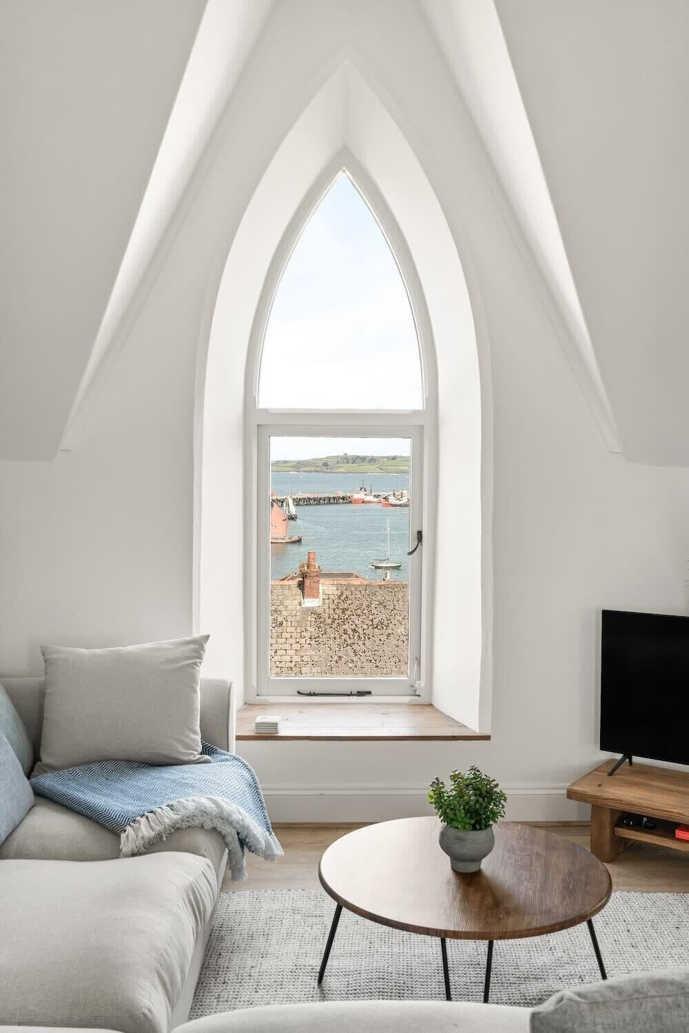 Une chambre de style loft moderne, dotée d’une grande fenêtre en arc d’où l’on a vue sur un port.