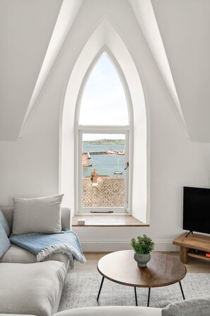 A modern loft bedroom with a large arched window overlooking a harbor.