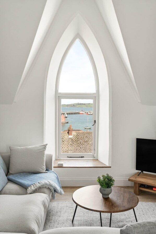 A modern loft bedroom with a large arched window overlooking a harbor.