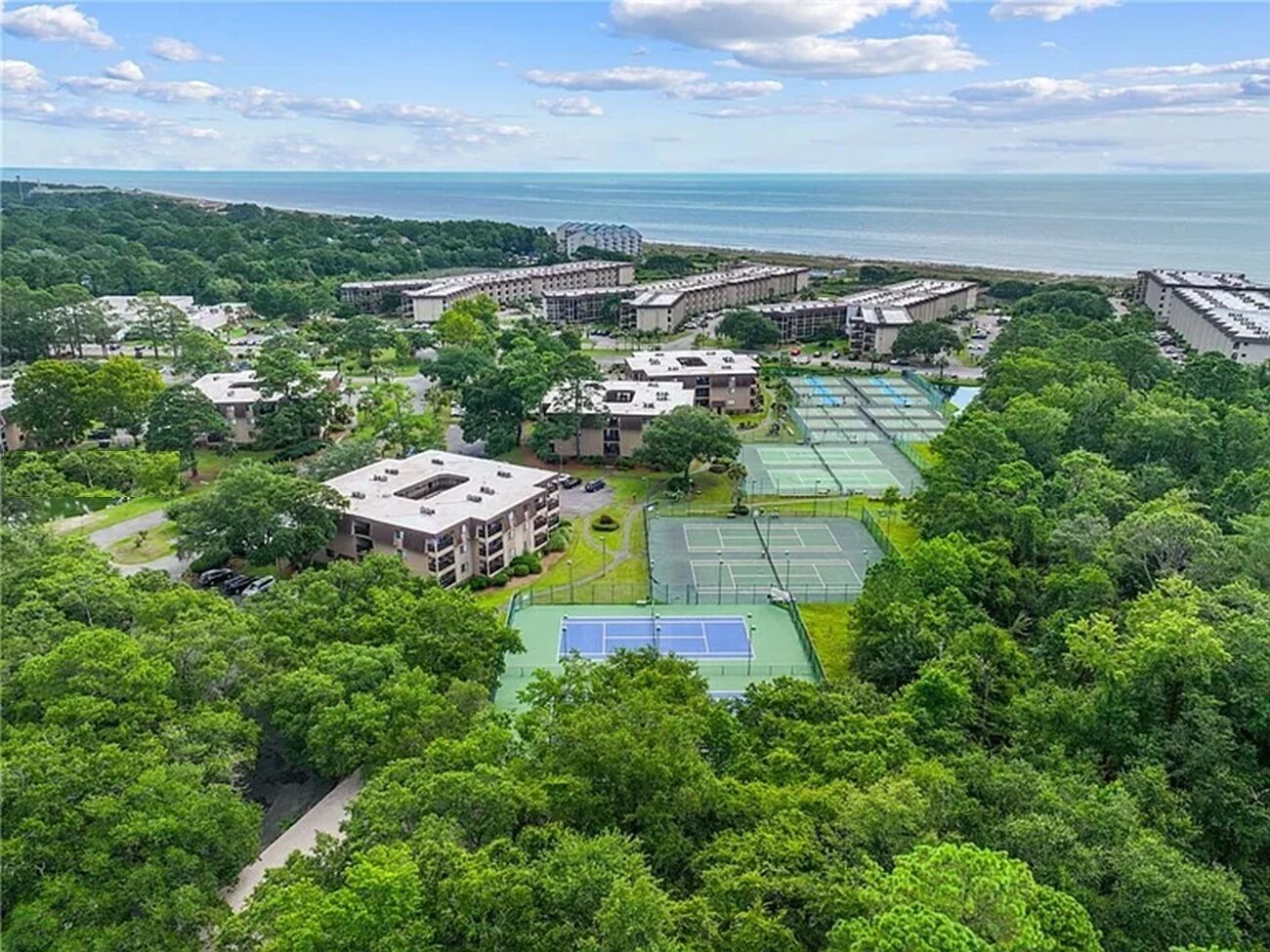 Vista aérea de una zona residencial con varios edificios de apartamentos, canchas de tenis y abundante vegetación.