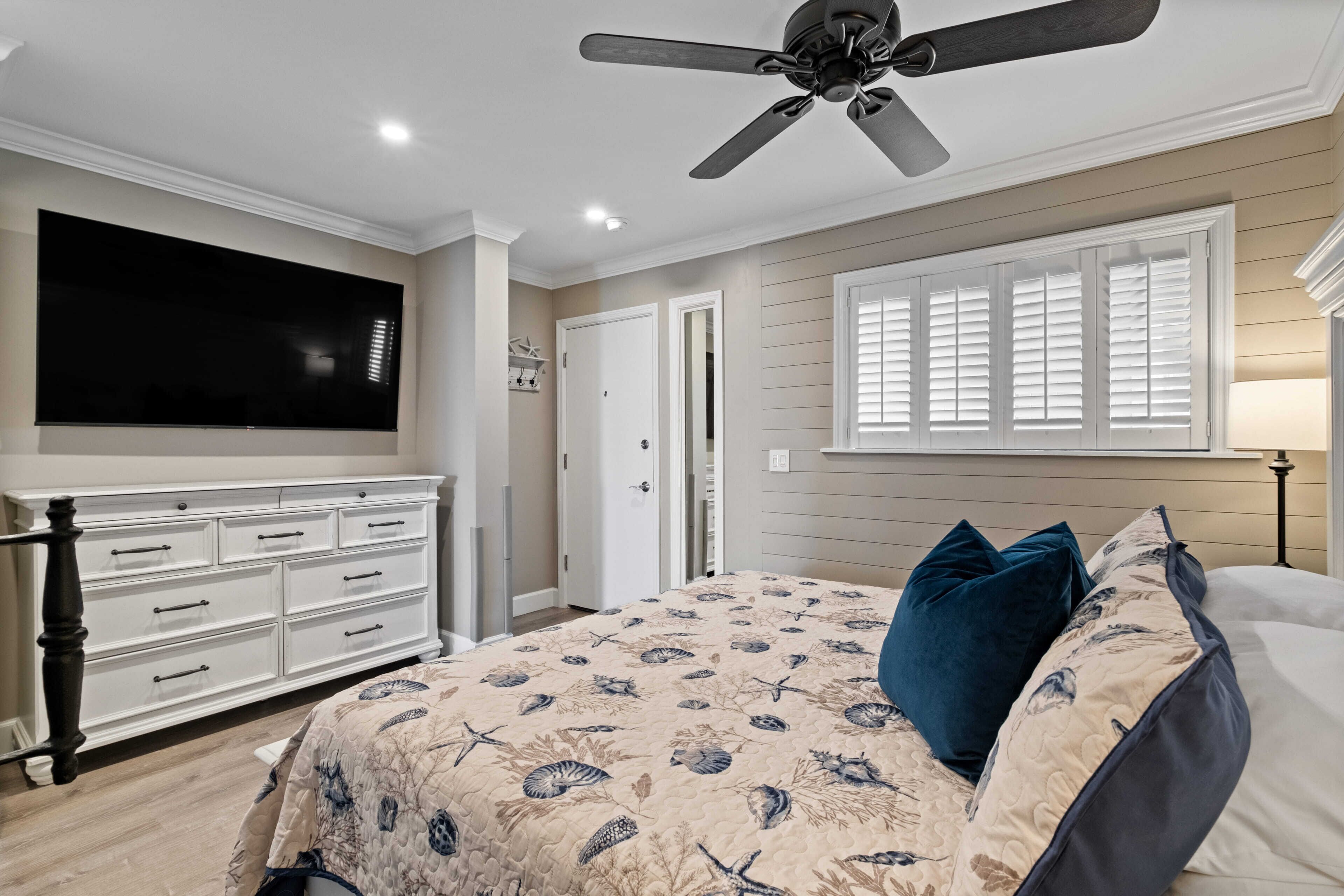 A bedroom with a bed, a ceiling fan, a TV, and a dresser.