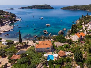 Vista aérea de una zona costera con aguas azules cristalinas, barcos y casas con tejados rojos.
