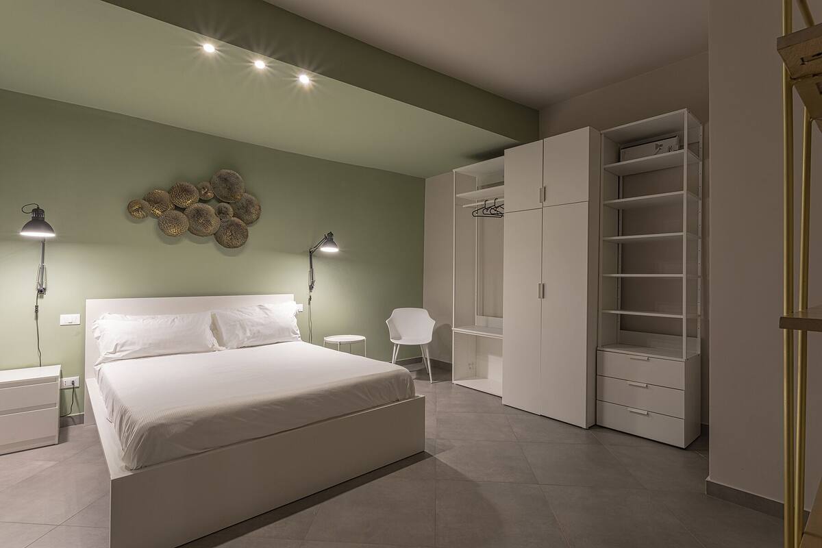 A bedroom with a bed, bedside lamps, a wardrobe, and a chair.