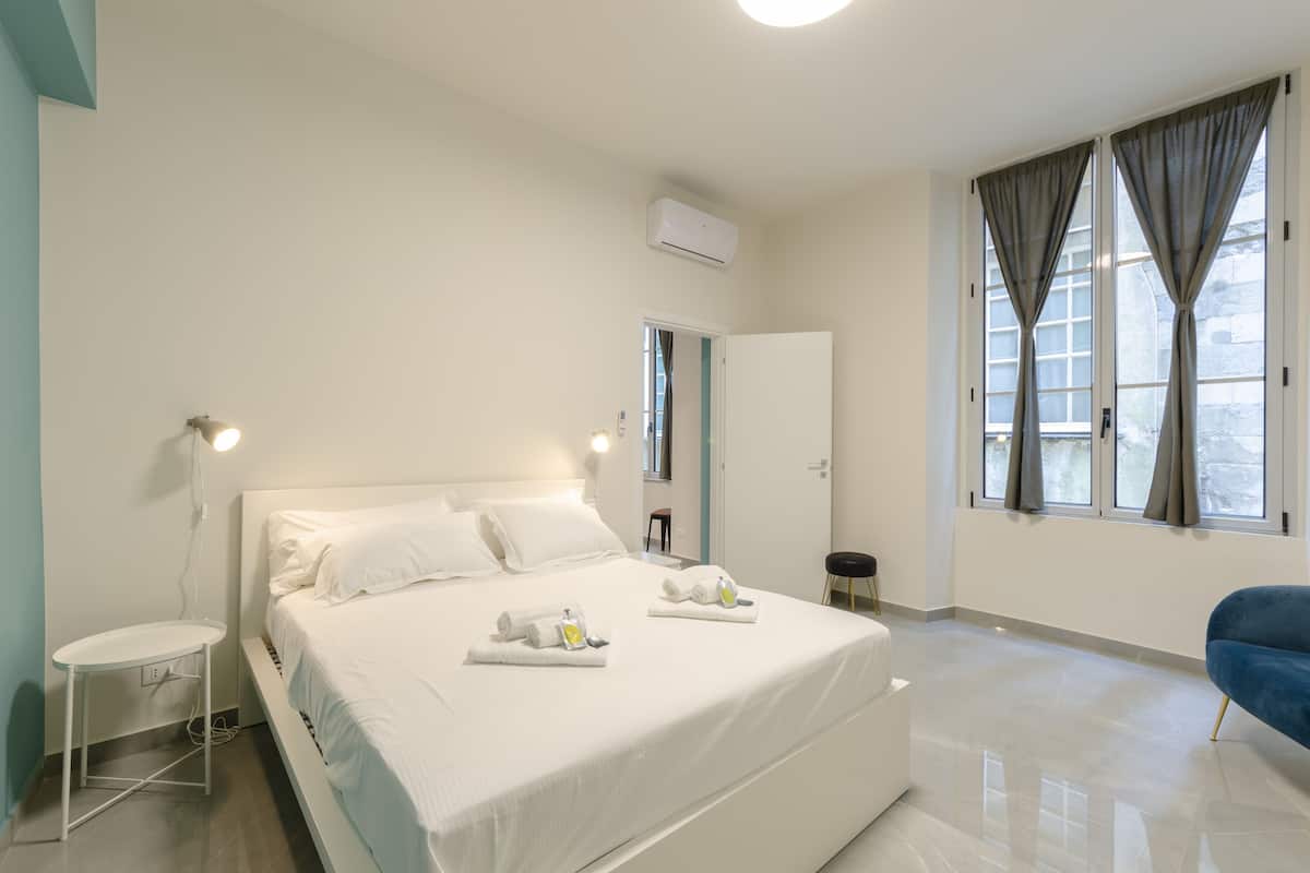 A modern bedroom with a large bed, bedside tables, a wardrobe, and a window with curtains.