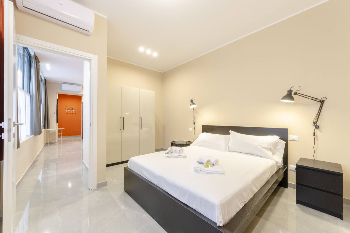 A modern hotel room with a large bed, bedside tables, a desk, and a wardrobe.