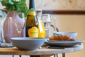 Una mesa con un croissant, una botella de Prosecco y diferentes vasos.