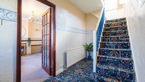 A staircase with patterned carpet leading to a room with a fireplace and a chandelier. - Melrose 1 (Lancaster)