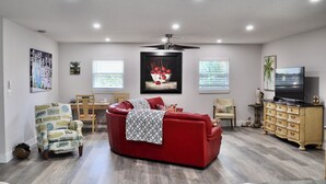 A spacious living room with a red sofa, a dining area with a wooden table and chairs, and a TV on a wooden cabinet.