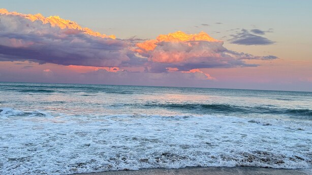 A beach with waves and a sunset sky.