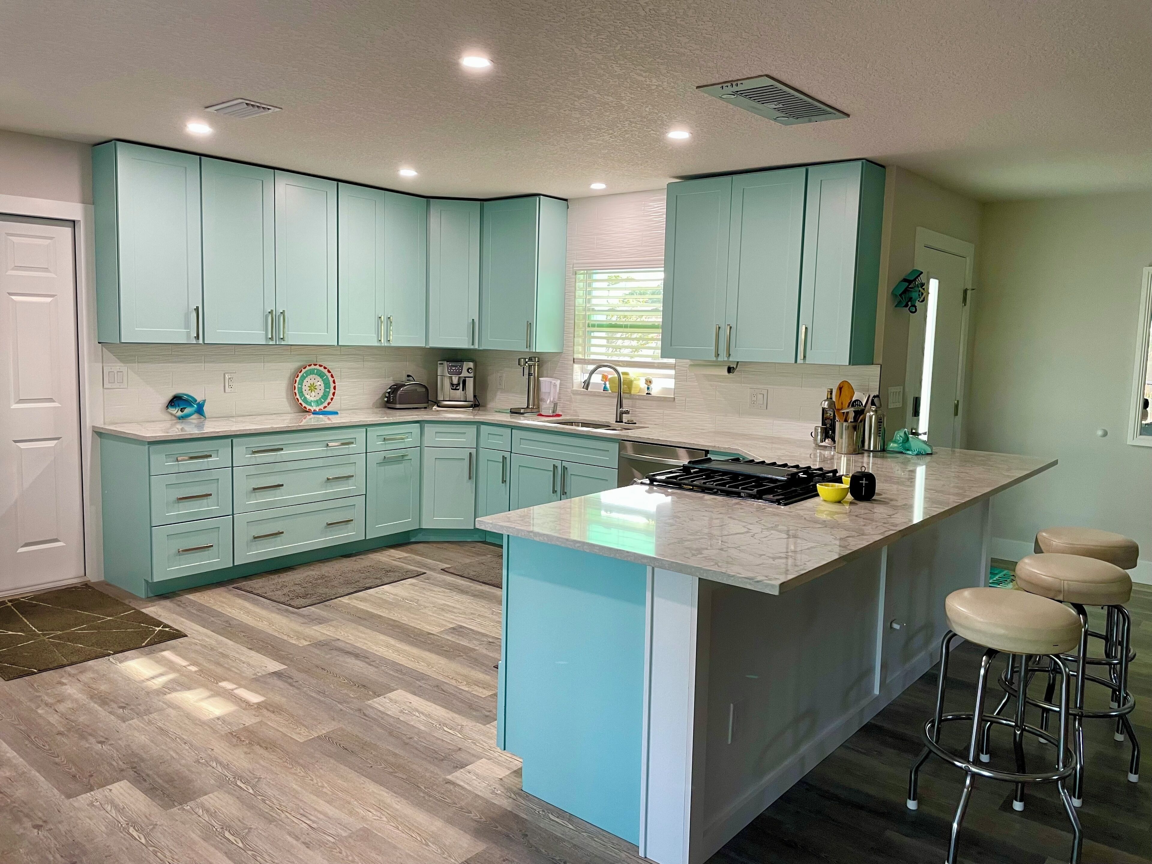 A modern kitchen with teal cabinetry, a central island, and bar stools.