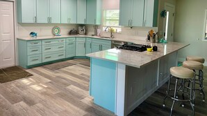 A modern kitchen with teal cabinetry, a central island, and bar stools.