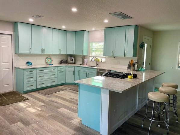 A modern kitchen with teal cabinetry, a central island, and bar stools.