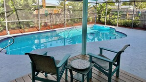 A covered outdoor swimming pool with a wooden deck, two chairs, and a table.