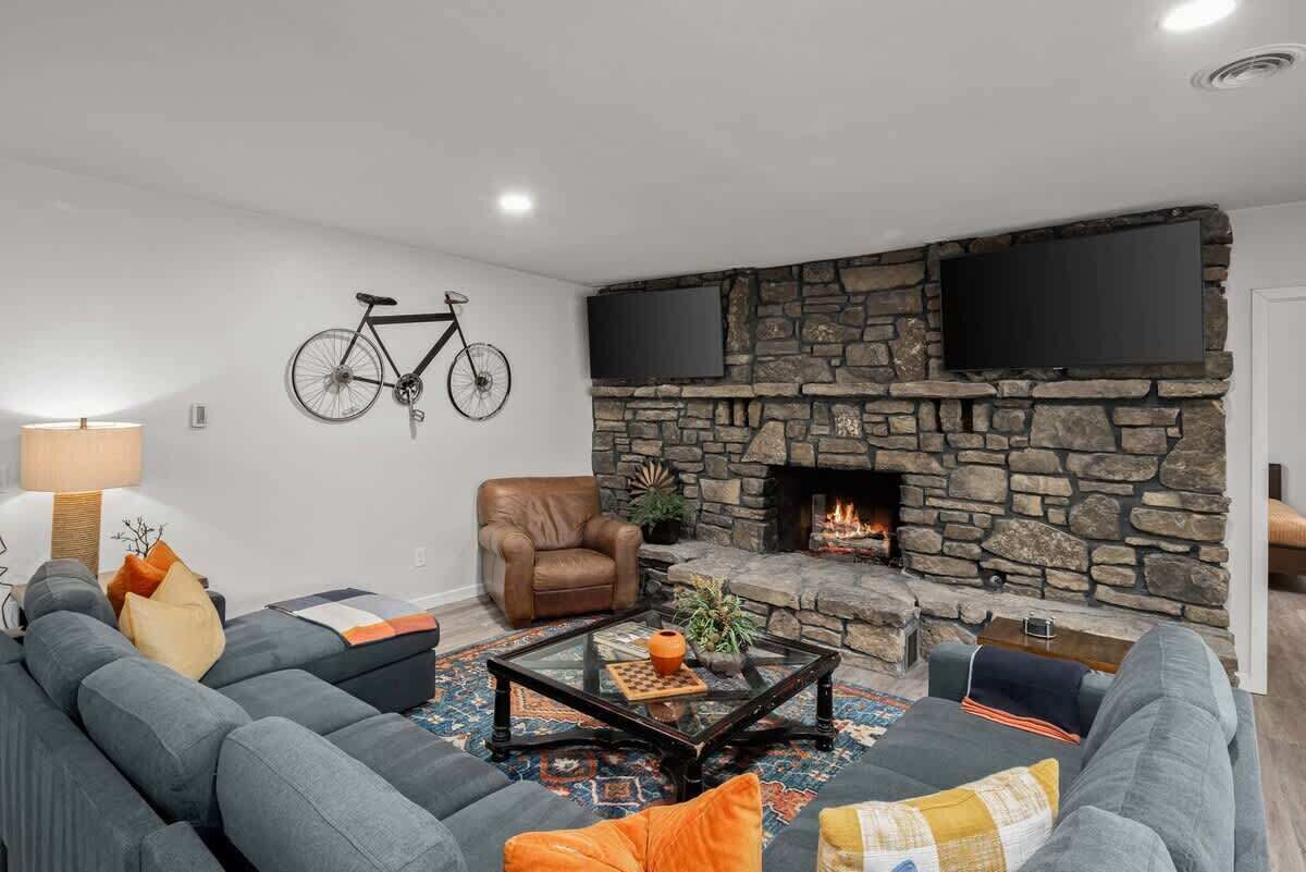A living room with a stone fireplace, a mounted television, a bicycle, and a leather armchair.