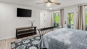 Un dormitorio con cama, ventilador de techo, televisor montado y vista al exterior.