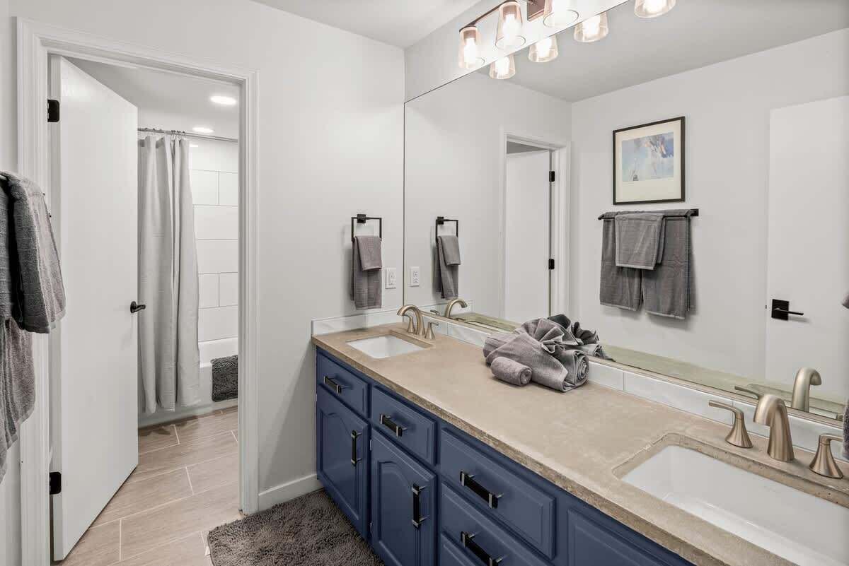 A modern bathroom with a large mirror, two sinks, and a walk-in shower.
