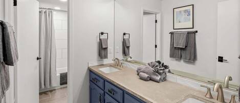 A modern bathroom with a large mirror, two sinks, and a walk-in shower.