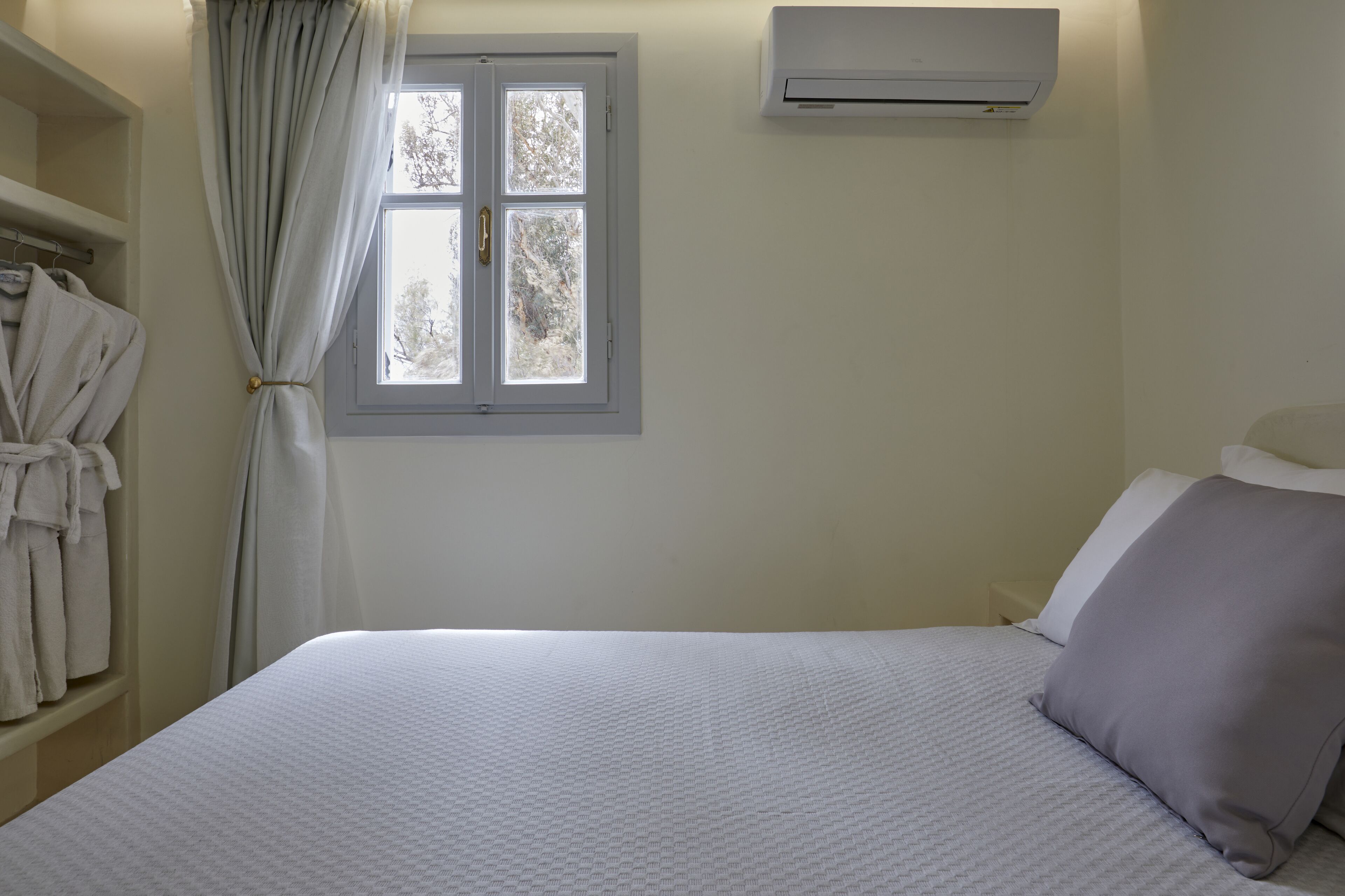 Une chambre à coucher comprenant un lit, une fenêtre avec des rideaux, un appareil de climatisation et un porte-manteau.