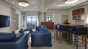 Un salon moderne avec un ensemble de canapés, un coin repas avec des tabourets de bar, une cuisine équipée d’un téléviseur et une vue sur la mer.