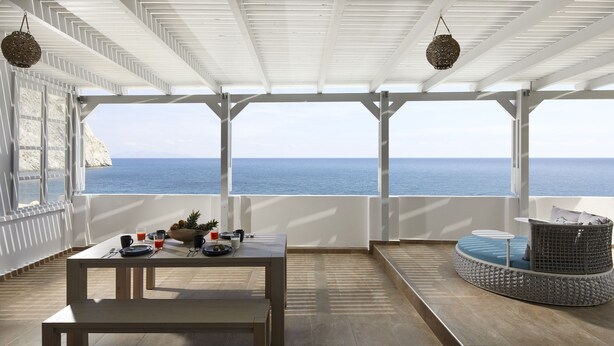 Un espace extérieur abrité, avec une table dressée pour les repas, un coin salon et une vue sur la mer.