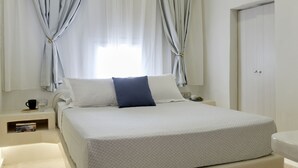 Une chambre moderne avec un grand lit, des tables de chevet, une commode et une salle de bain équipée de toilettes et d’un lavabo.
